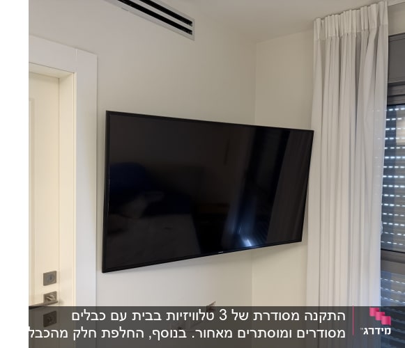 טלוויזיה מותקנת על קיר ליד חלון עם וילון לבן